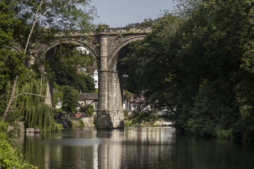 View of the historic Knaresborough Viaduct spanning the River Nidd surrounded by lush green trees and stone buildings in Knaresborough England United Kingdom.
