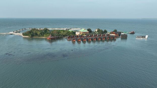 Aerial view of Pulau Lima Resort featuring rows of overwater bungalows on a small island surrounded by calm turquoise waters in Kasemen Banten Indonesia. Aerial view of Pulau Lima Resort featuring rows of overwater bungalows on a small island surrounded by calm turquoise waters in Kasemen Banten Indonesia.