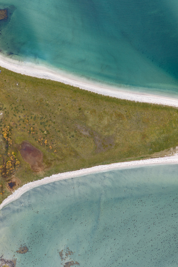 Aerial view of the Lofoten coastline in Svolvaer featuring a narrow grassy peninsula separating turquoise waters and sandy beaches in Svolvaer Nordland Norway.
