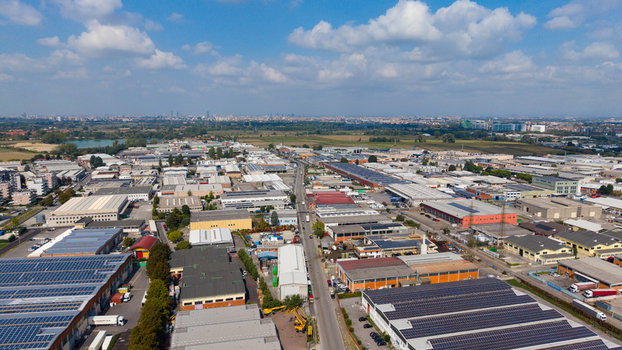 Aerial view of an industrial and logistics complex featuring warehouses with solar panels on rooftops surrounded by roads and green fields in San Giuliano Milanese Lombardy Italy. Aerial view of an industrial and logistics complex featuring warehouses with solar panels on rooftops surrounded by roads and green fields in San Giuliano Milanese Lombardy Italy.