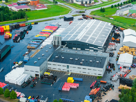 Jelgava Latvia 04 July 2026 Aerial view of an industrial pipe manufacturing facility with colorful plastic pipes stored outdoors a large warehouse and surrounding green landscape.