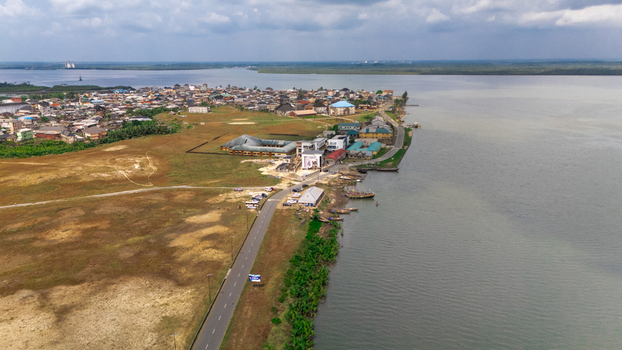 Aerial view of a coastal town with houses a road running along the shoreline and small boats moored in the river in Rivers Nigeria.