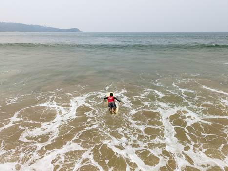 Aerial view of a surfer paddling on a surfboard through white foam waves near Dewata Beach Road Galle Southern Province Sri Lanka.
