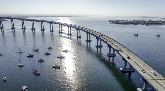 Aerial view of the Coronado Bridge crossing San Diego Bay with sailboats anchored in the water below under a clear sky in San Diego CA United States. Aerial view of the Coronado Bridge crossing San Diego Bay with sailboats anchored in the water below under a clear sky in San Diego CA United States.