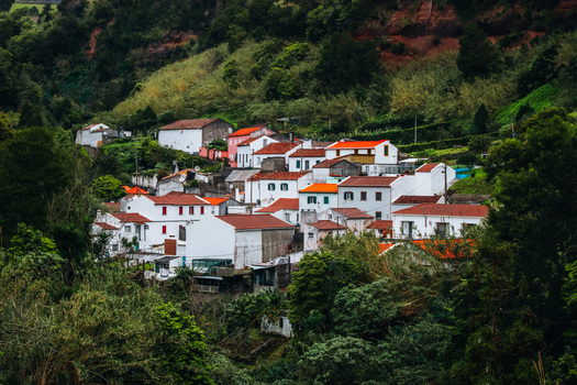 View of white houses with terracotta roofs nestle amidst lush green hills a vibrant splash of color against the verdant landscape Furnas Azores Portugal.