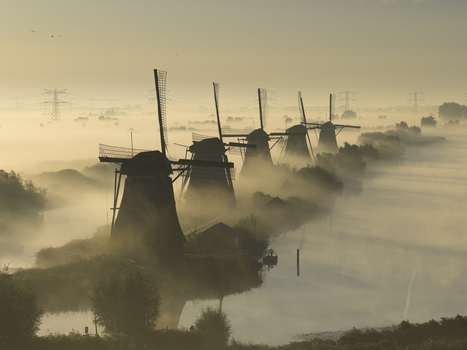 Aerial view of historic windmills at the UNESCO World Heritage site emerging from thick morning mist over the water Kinderdijk Zuid Holland Netherlands.
