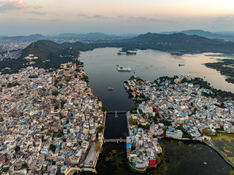 Aerial view of the historic city of Udaipur with its dense urban landscape the expansive Lake Pichola and the iconic City Palace complex nestled among hills in Udaipur Rajasthan India.