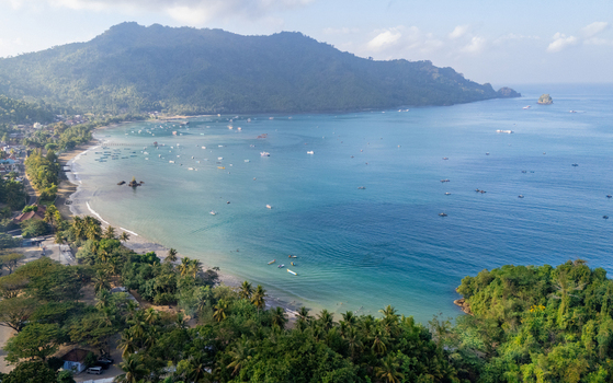 Aerial view of Prigi Beach with turquoise waters small fishing boats lush coastal hills and palm trees along the sandy shoreline in Kecamatan Watulimo Jawa Timur Indonesia. Aerial view of Prigi Beach with turquoise waters small fishing boats lush coastal hills and palm trees along the sandy shoreline in Kecamatan Watulimo Jawa Timur Indonesia.