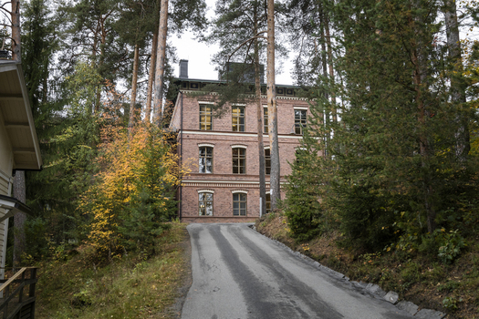 View of a historic red brick building nestled among tall pine trees in a forest setting with a paved driveway leading up to the entrance in Jyvaskyla Central Finland Finland.