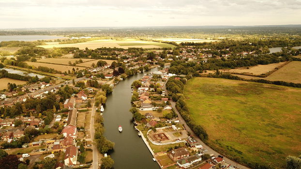 Aerial view of the Thames River winding through a residential area with lush green fields trees and small boats in Thames United Kingdom. Aerial view of the Thames River winding through a residential area with lush green fields trees and small boats in Thames United Kingdom.