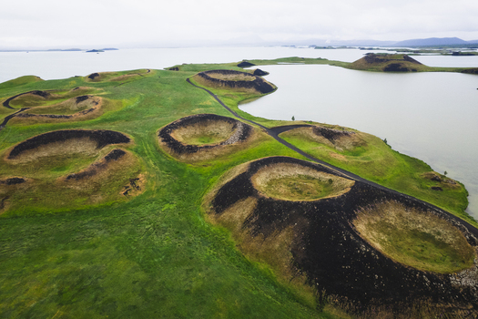 Aerial view of pseudocraters punctuate the vibrant green landscape along the tranquil lake s edge creating a striking contrast between earth and water Skutustadagigar Lake Myvatn Iceland.