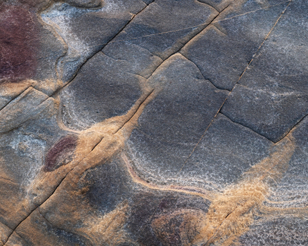 View of the intricate texture and natural patterns of weathered coastal rocks with deep cracks and mineral veins Calafuria Toscana Italy.
