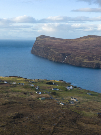 Aerial view of the coastal village of Milovaig with scattered white houses on green slopes overlooking the blue sea and dramatic cliffs Milovaig Scotland United Kingdom.