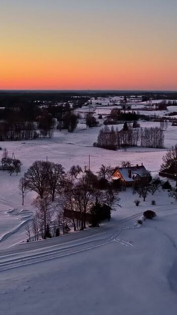 Aerial view of snowy rural landscape at sunset in Latvia.