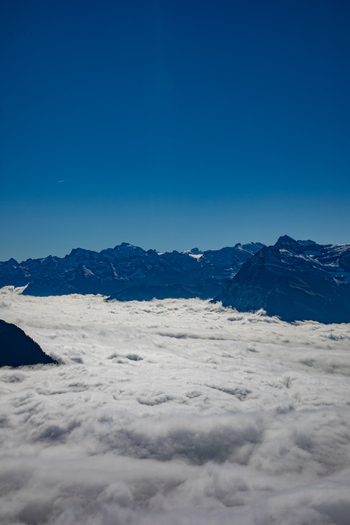 Aerial view of the Swiss Alps rising above a thick blanket of clouds under a clear blue sky in Airolo Ticino Switzerland. Aerial view of the Swiss Alps rising above a thick blanket of clouds under a clear blue sky in Airolo Ticino Switzerland.
