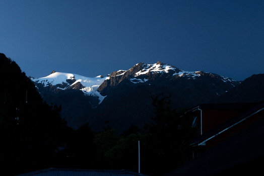 View of snow capped mountains gleaming under a bright sky casting long shadows over the landscape a serene vista Franz Josef Glacier West Coast Region New Zealand. View of snow capped mountains gleaming under a bright sky casting long shadows over the landscape a serene vista Franz Josef Glacier West Coast Region New Zealand.