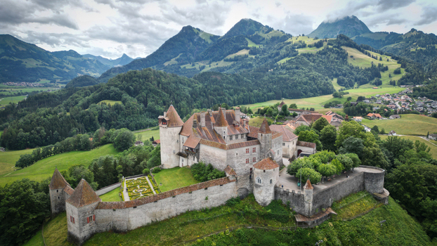 Aerial view of an ancient castle with red roofs and stone walls atop a green hill against a backdrop of majestic mountains Gruy&egrave;res Fribourg Switzerland.