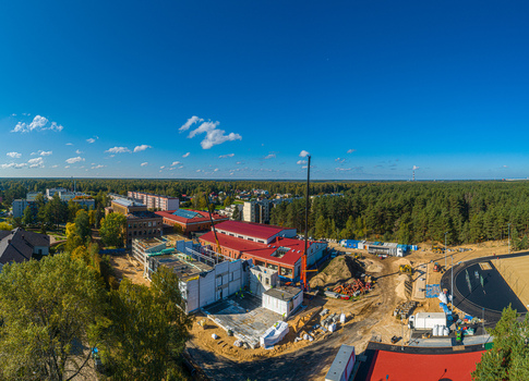 Aerial view of a construction site featuring a building with a red roof cranes and a new running track surrounded by a dense forest in Latvia. Aerial view of a construction site featuring a building with a red roof cranes and a new running track surrounded by a dense forest in Latvia.