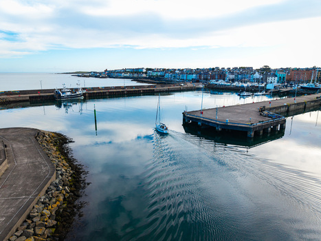 Aerial view of Bangor Harbour and Town with a sailboat navigating the calm waters between stone piers and coastal buildings in Bangor Northern Ireland United Kingdom.