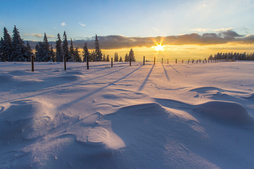 View of a snow covered field with stark shadows cast by a rustic fence under a vibrant sunset sky painting the landscape in warm and cool hues Schöckl Styria Austria. View of a snow covered field with stark shadows cast by a rustic fence under a vibrant sunset sky painting the landscape in warm and cool hues Schöckl Styria Austria.