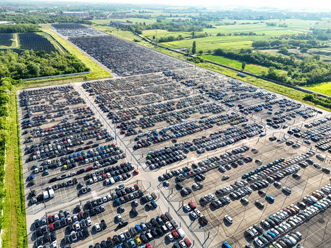 Aerial view of a massive car storage facility with thousands of vehicles parked in rows surrounded by green fields in Rivalta di Torino Piedmont Italy. Aerial view of a massive car storage facility with thousands of vehicles parked in rows surrounded by green fields in Rivalta di Torino Piedmont Italy.