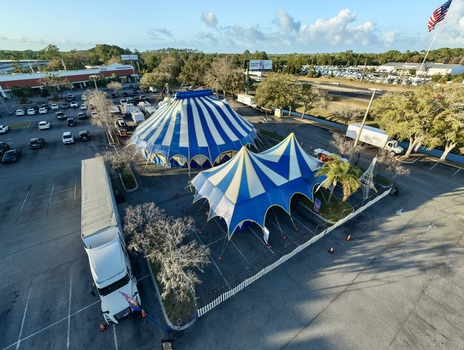 Aerial view of blue and white striped circus tents standing boldly on the asphalt a stark contrast to the surrounding green trees and distant buildings St. Augustine Florida United States. Aerial view of blue and white striped circus tents standing boldly on the asphalt a stark contrast to the surrounding green trees and distant buildings St. Augustine Florida United States.