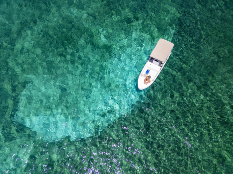 Aerial view of a small white motorboat with a canopy floating on crystal clear turquoise water over a coral reef with a person on board Guanaja Bay Islands Department Honduras. Aerial view of a small white motorboat with a canopy floating on crystal clear turquoise water over a coral reef with a person on board Guanaja Bay Islands Department Honduras.