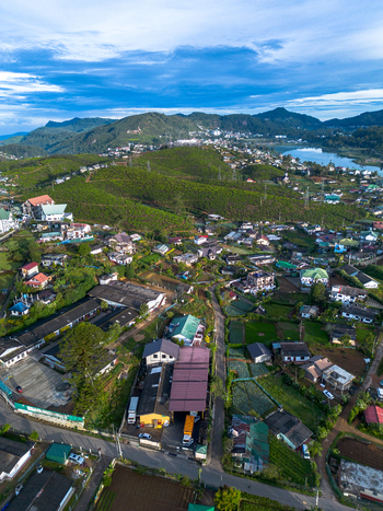 Aerial view of Nuwara Eliya town nestled among tea plantations and rolling hills with a lake and scattered buildings under a blue sky in Nuwara Eliya Central Province Sri Lanka. Aerial view of Nuwara Eliya town nestled among tea plantations and rolling hills with a lake and scattered buildings under a blue sky in Nuwara Eliya Central Province Sri Lanka.
