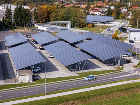 Aerial view of solar panel carports in a parking lot with parked cars and surrounding autumn trees in Slovenia.