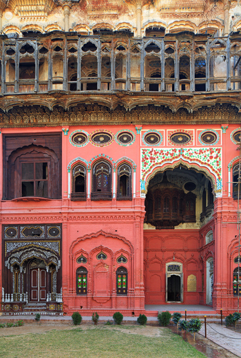 View of the ornate red facade of the historic Umar Hayat Mahal Library featuring intricate wooden balconies carved arches and decorative patterns in Chiniot Punjab Pakistan.