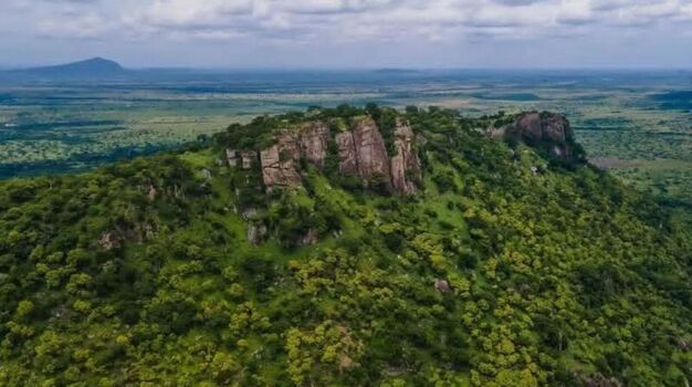 Aerial view of a rocky hill covered in lush green vegetation rising above the surrounding savanna landscape in Ghana. Aerial view of a rocky hill covered in lush green vegetation rising above the surrounding savanna landscape in Ghana.