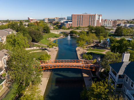 Aerial view of the Indianapolis Canal Walk with its orange pedestrian bridge fountain lush trees and urban buildings in Indianapolis Indiana United States. Aerial view of the Indianapolis Canal Walk with its orange pedestrian bridge fountain lush trees and urban buildings in Indianapolis Indiana United States.
