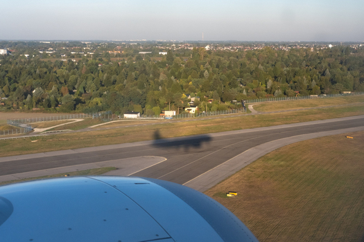Aerial view of an airplane s shadow cast dramatically over the runway as it prepares for landing amidst a backdrop of verdant trees Warsaw Masovian Voivodeship Poland. Aerial view of an airplane s shadow cast dramatically over the runway as it prepares for landing amidst a backdrop of verdant trees Warsaw Masovian Voivodeship Poland.