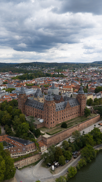 Aerial view of Schloss Johannisburg a historic red sandstone Renaissance castle overlooking the river Main surrounded by lush trees and the cityscape of Aschaffenburg Bayern Germany.