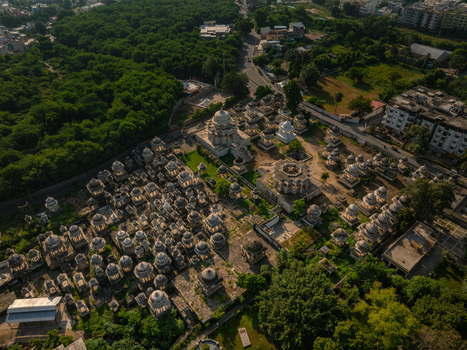Aerial view of the historic Ahar Cenotaphs featuring numerous white marble domes and intricate stone structures surrounded by lush green trees in Udaipur Rajasthan India.