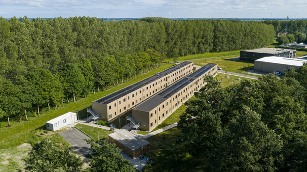 Aerial view of modular housing units surrounded by lush green trees and open fields in Middenmeer North Holland Netherlands.
