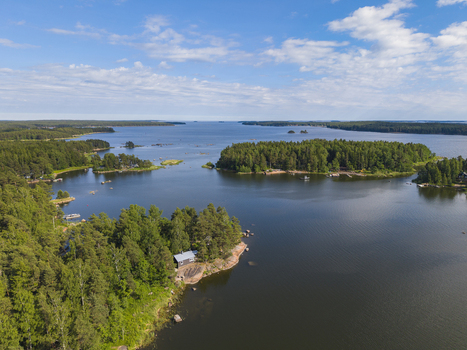 Aerial view of a wooden cottage nestled in dense pine forests on a rocky island in the Finnish archipelago surrounded by calm blue waters in Hamina Kymenlaakso Finland. Aerial view of a wooden cottage nestled in dense pine forests on a rocky island in the Finnish archipelago surrounded by calm blue waters in Hamina Kymenlaakso Finland.