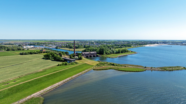 Aerial view of the historic Wouda pumping station with its iconic chimney surrounded by lush green fields dikes and the waters of the IJsselmeer in Lemmer Friesland Netherlands.