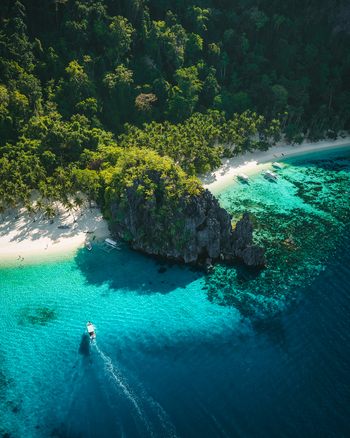 Aerial view of Papaya Beach with turquoise waters coral reefs a rocky outcrop lush tropical forest and a small boat in El Nido Mimaropa Philippines. Aerial view of Papaya Beach with turquoise waters coral reefs a rocky outcrop lush tropical forest and a small boat in El Nido Mimaropa Philippines.