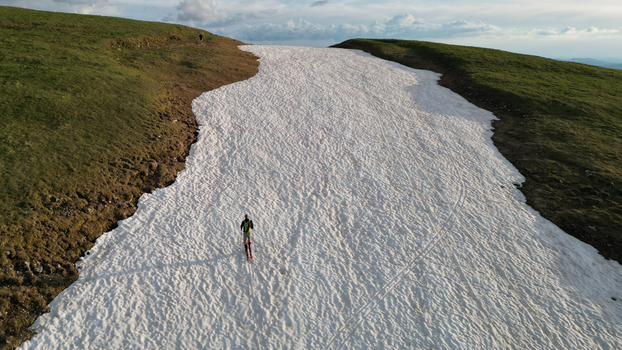Aerial view of a skier descending a narrow snow patch on the grassy slopes of Le Colomby de Gex under a cloudy sky Echenevex Auvergne Rhone Alpes France. Aerial view of a skier descending a narrow snow patch on the grassy slopes of Le Colomby de Gex under a cloudy sky Echenevex Auvergne Rhone Alpes France.