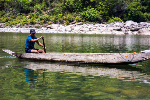 Meghalaya India 31 March 2023 View of a man rowing a traditional wooden boat on the clear green river with rocky banks and lush forest in the background. Meghalaya India 31 March 2023 View of a man rowing a traditional wooden boat on the clear green river with rocky banks and lush forest in the background.