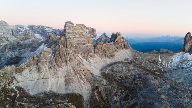 Aerial view of the Tre Cime di Lavaredo peaks with jagged rock formations and scree slopes under a soft dawn sky in Auronzo di Cadore Veneto Italy. Aerial view of the Tre Cime di Lavaredo peaks with jagged rock formations and scree slopes under a soft dawn sky in Auronzo di Cadore Veneto Italy.