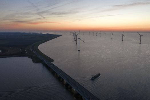 Aerial view of Ketelbrug bridge and offshore wind turbines at sunset with a cargo ship on the water in Nagele Flevoland Netherlands.