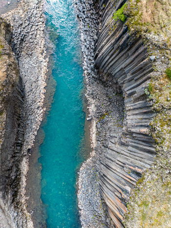 Aerial view of the turquoise river flowing through the dramatic basalt columns of Studlagil Canyon in Iceland. Aerial view of the turquoise river flowing through the dramatic basalt columns of Studlagil Canyon in Iceland.