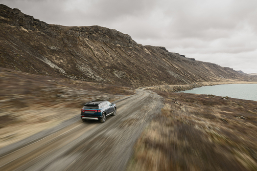 Aerial view of a car driving along a gravel road beside Hlidarvatn lake surrounded by rugged hills and dramatic landscape in Sveitarfelagid Olfus Iceland. Aerial view of a car driving along a gravel road beside Hlidarvatn lake surrounded by rugged hills and dramatic landscape in Sveitarfelagid Olfus Iceland.