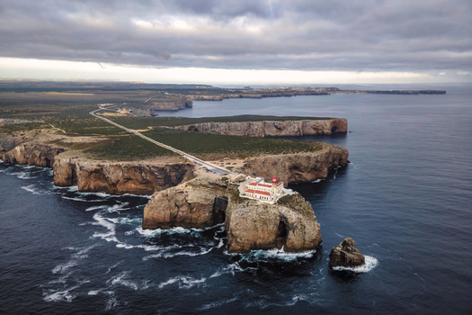 Aerial view of Farol do Cabo de Sao Vicente a beautiful lighthouse on the cliff at sunset facing the ocean Sagres Algarve region Portugal.