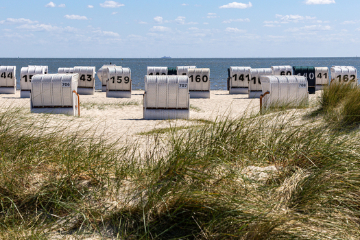 View of Strand Schillig with numbered white hooded beach chairs on the sand and green dunes under a blue sky in Wangerland Niedersachsen Germany. View of Strand Schillig with numbered white hooded beach chairs on the sand and green dunes under a blue sky in Wangerland Niedersachsen Germany.