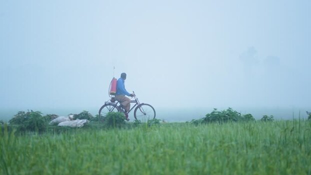 View of a farmer on a bicycle in a foggy field Bangladesh.