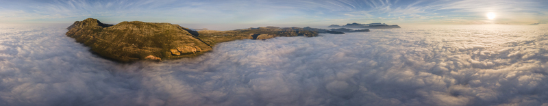 Aerial view of rugged mountains piercing through a sea of clouds kissed by the golden glow of the rising sun Cape Town Western Cape South Africa.