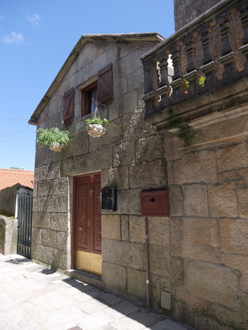 View of a traditional stone house with wooden shutters hanging flower pots and an ornate balcony in the historic village of Combarro Pontevedra Spain.